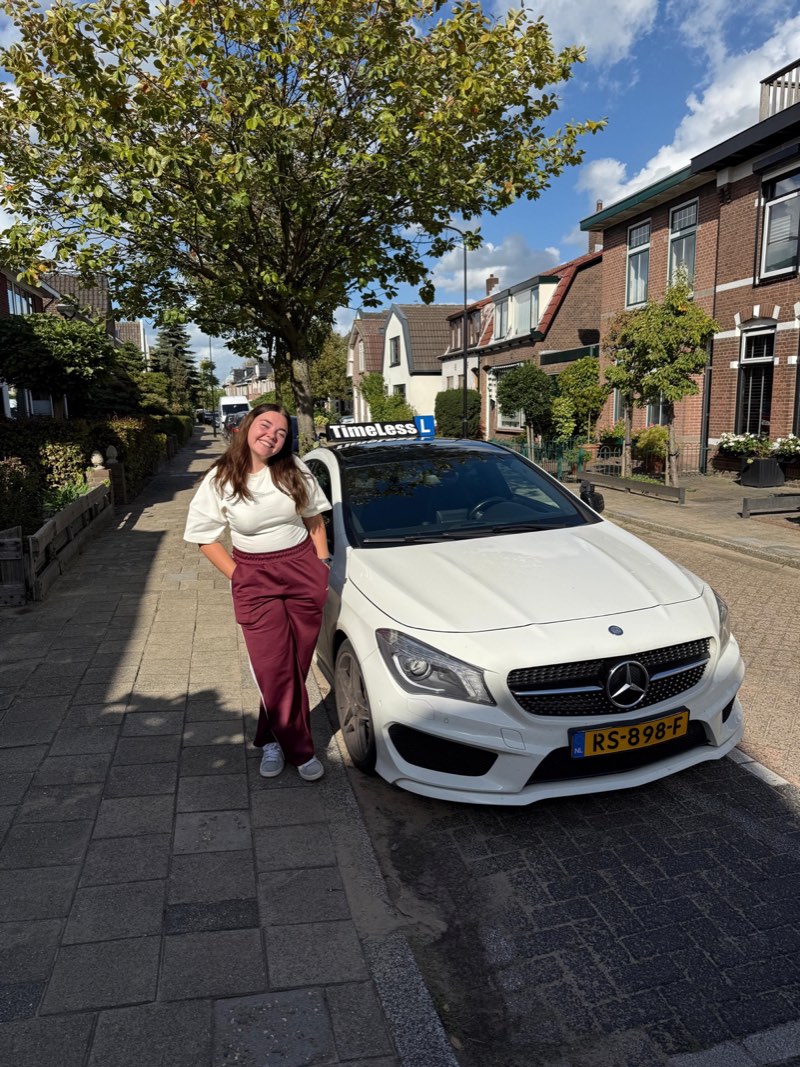 Geslaagde leerling bij de witte lesauto in de zon