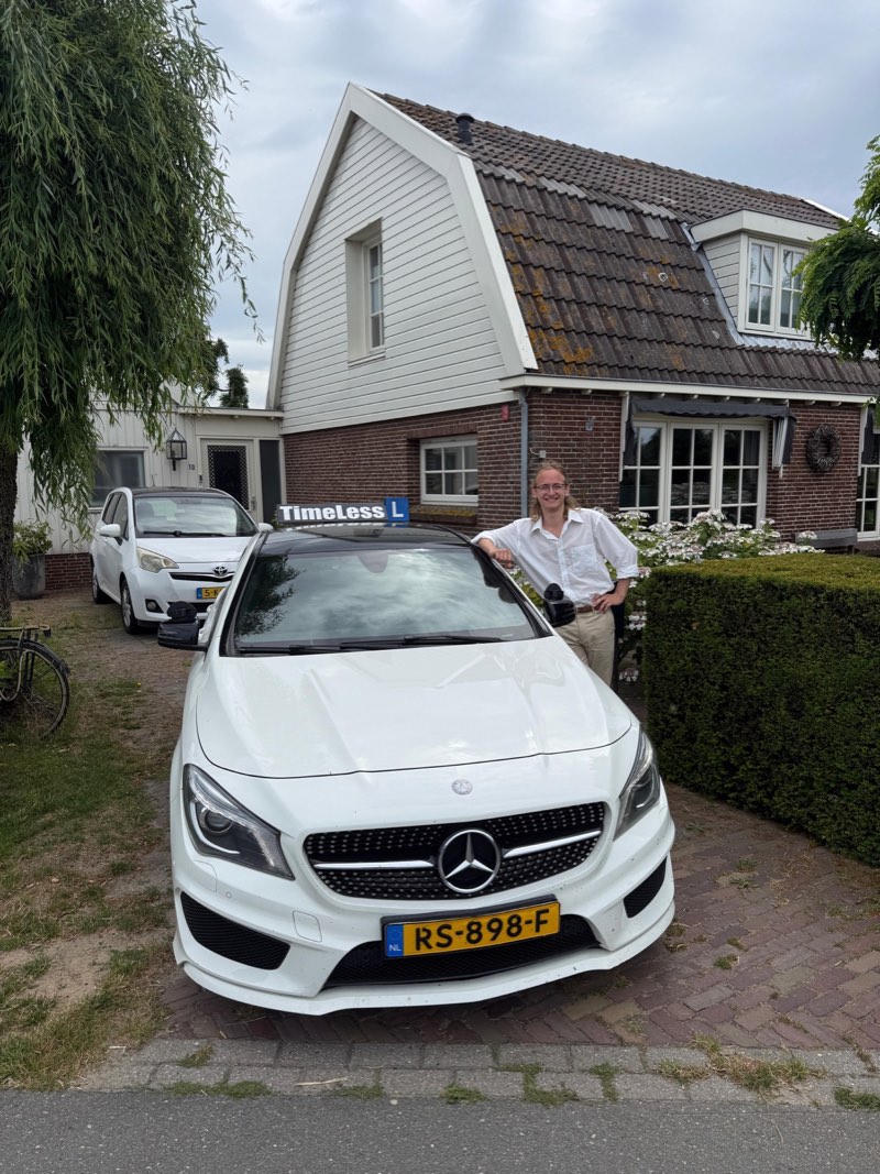 Geslaagde leerling leunt naast de lesauto