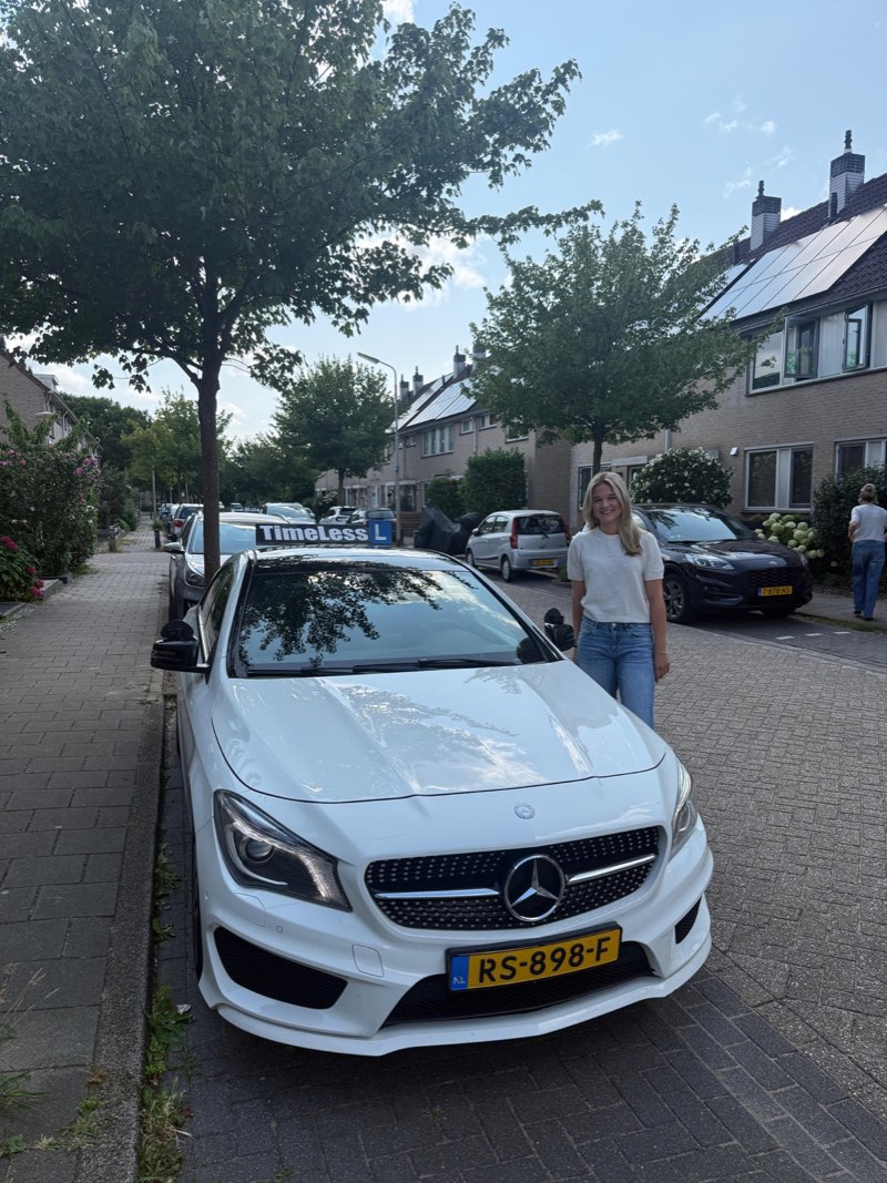 Geslaagde leerling naast de lesauto in een woonwijk